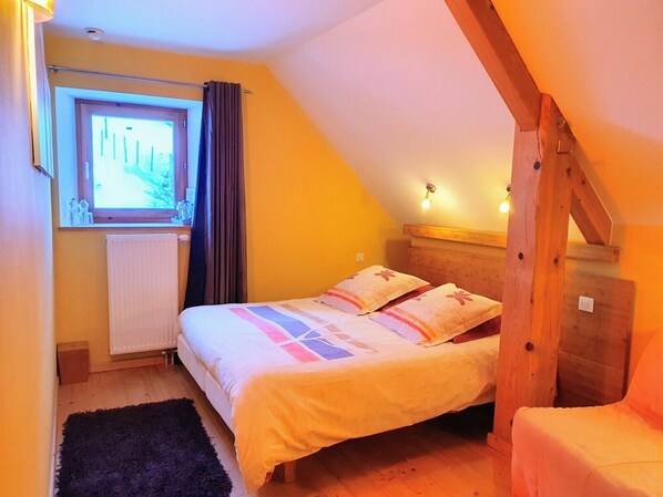 Un dormitorio acogedor con cama, ventana, radiador y escalera de madera.