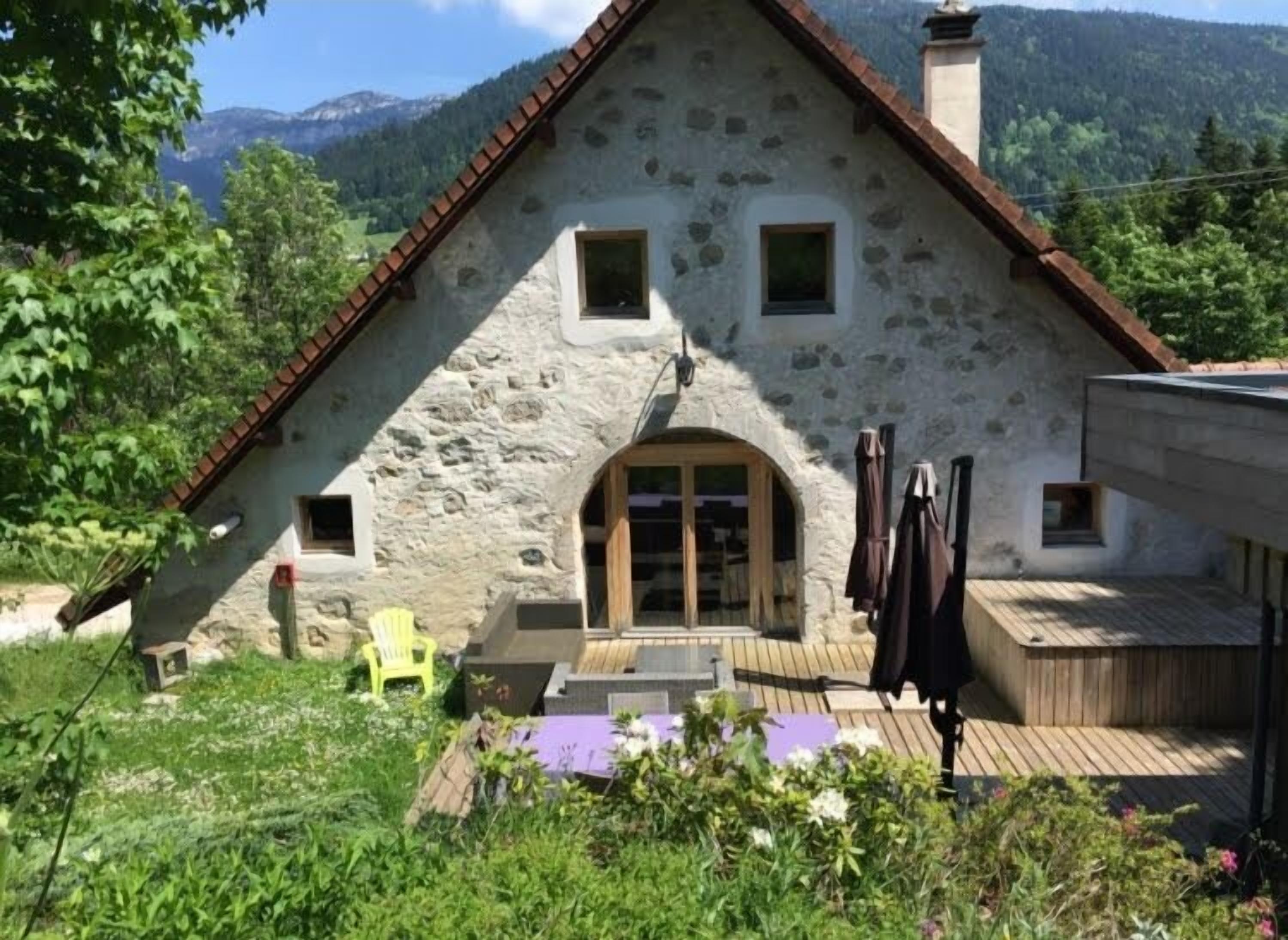 Une maison en pierre avec un toit en pente, une terrasse en bois et un petit jardin.