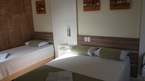 A hotel room with two single beds, a wooden headboard, a bedside table with a lamp, and artwork on the walls. - Hotel Mariani (Lajeado)