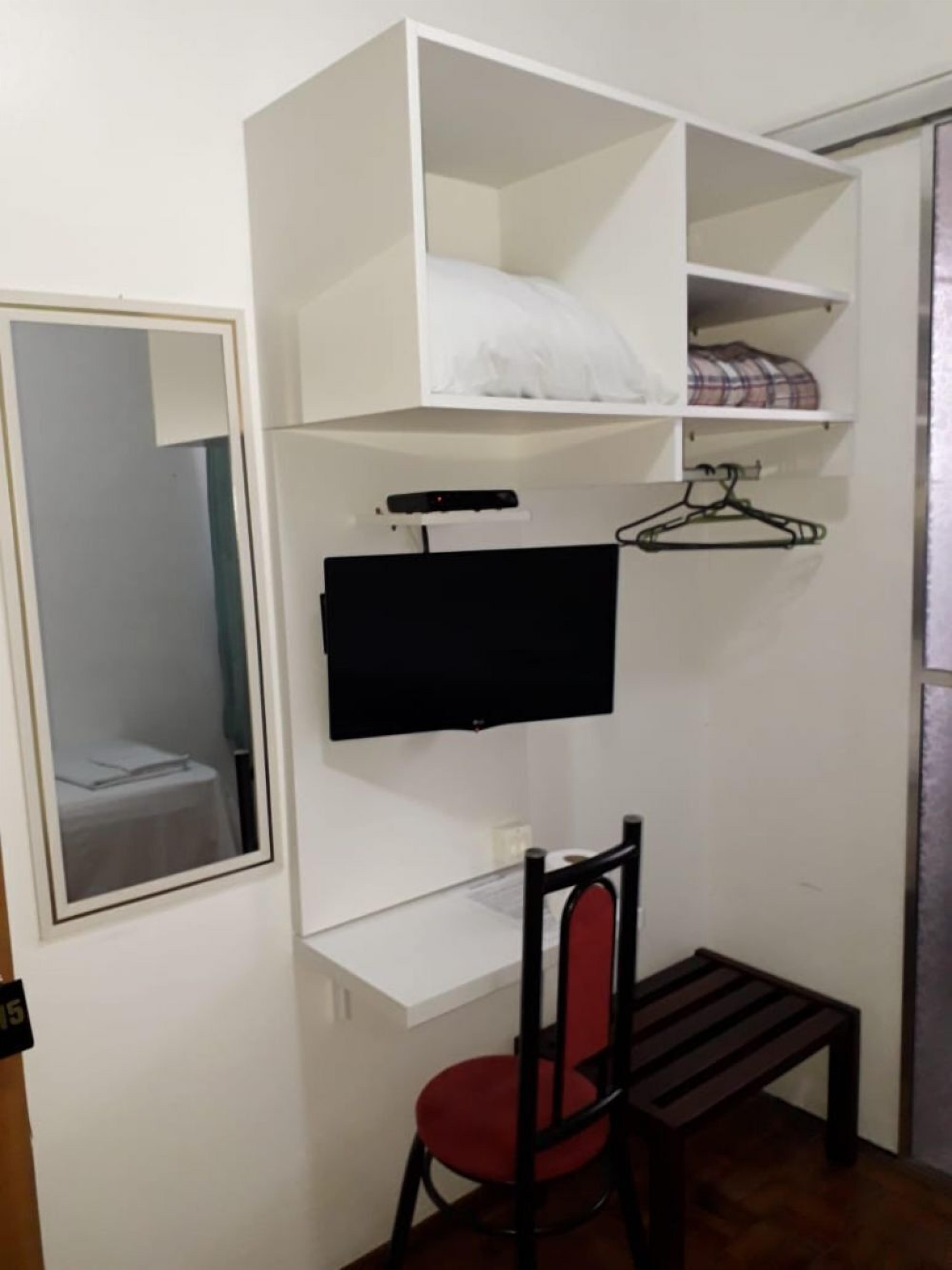 Quarto compacto com cama, escrivaninha, cadeira, televisão e guarda-roupa.