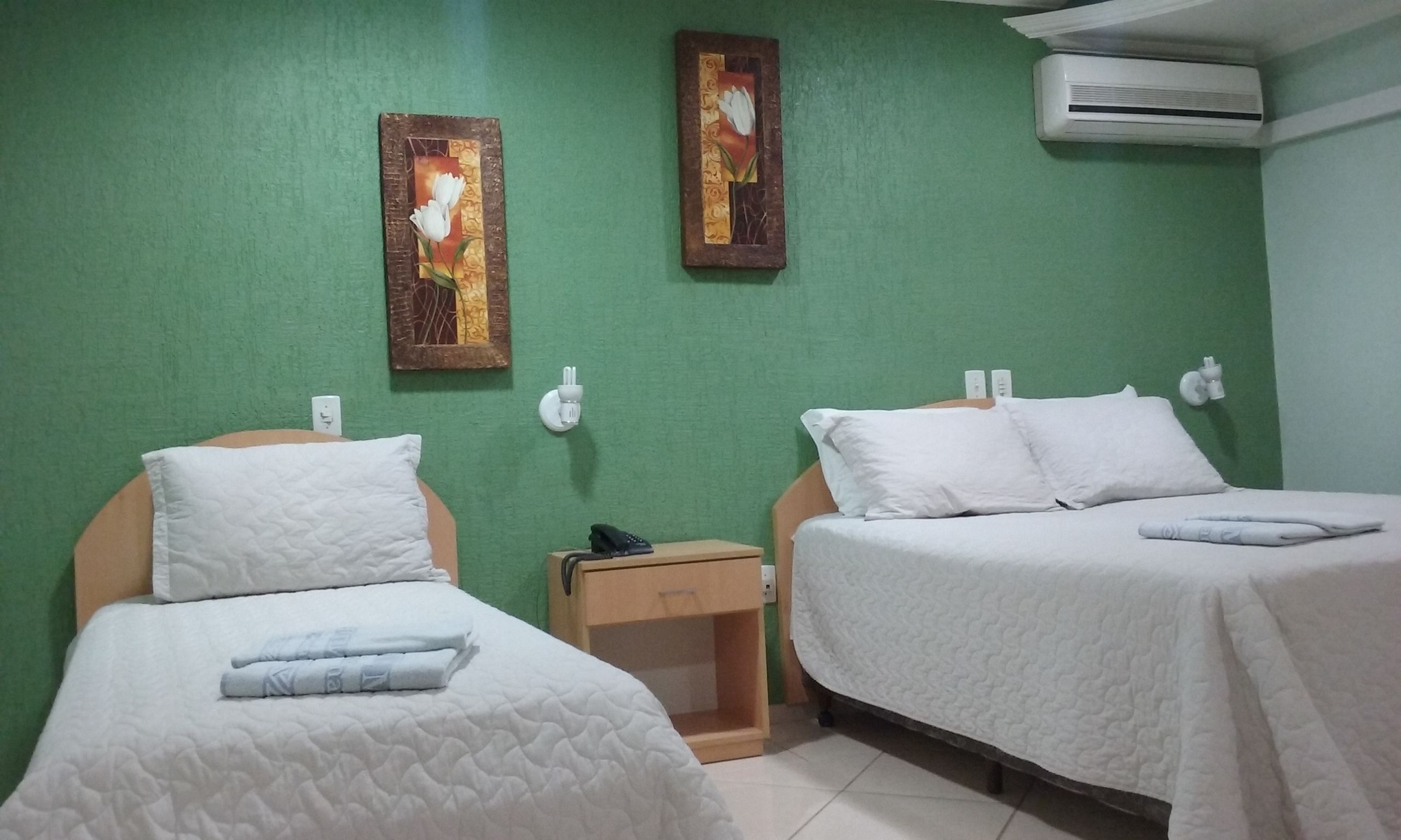 Habitación de hotel con dos camas, paredes verdes y dos cuadros de flores.