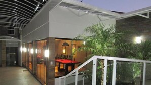 A modern indoor area with a pool table, a staircase, and a glass-enclosed room with a red table. - Hotel Mariani (Lajeado)