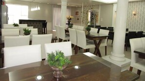 A dining area with white chairs, a wooden table, and a central plant. - Hotel Mariani (Lajeado)