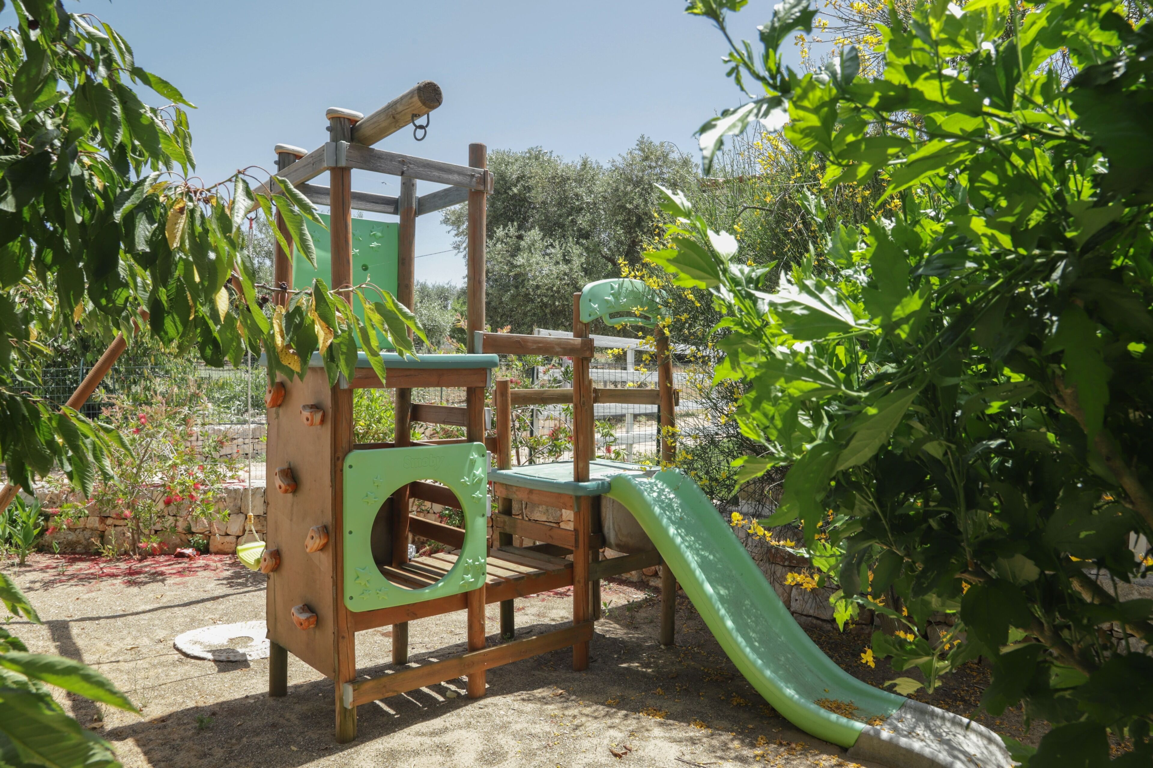 A wooden play structure with a slide and climbing elements in a garden setting.