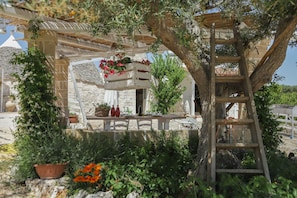 Un edificio in pietra con una pergola in legno, piante in vaso e una scala.