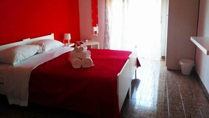 A hotel room with a red wall, a bed with white linens, a red bedspread, and a stack of rolled towels on the bed. - B&B La Bussola (Pachino)