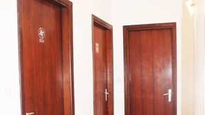 A hallway with three wooden doors, each with a handle and a small logo on the upper left corner. The floor is tiled with a light-colored pattern. - B&B La Bussola (Pachino)