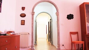 A hallway with a pink wall, a wooden cabinet, a radiator, and a chair. - B&B La Bussola (Pachino)
