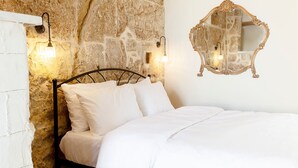 Ein Bett mit weißer Bettwäsche, eine Steinwand und ein Spiegel mit aufwendiger Rahmung.