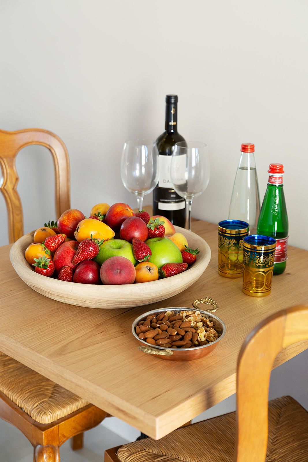 Una taula de fusta amb un plat de fruita, una ampolla de vi, gots i ampolles de refresc.