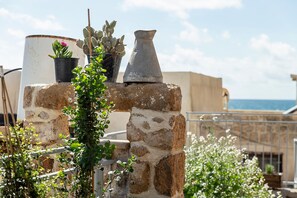 Un jardín en la azotea con plantas en macetas, un florero metálico y un muro de piedra.