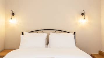 A bed with a black metal frame, two white pillows, and a white bedspread. There are two wall-mounted light fixtures on either side of the bed.