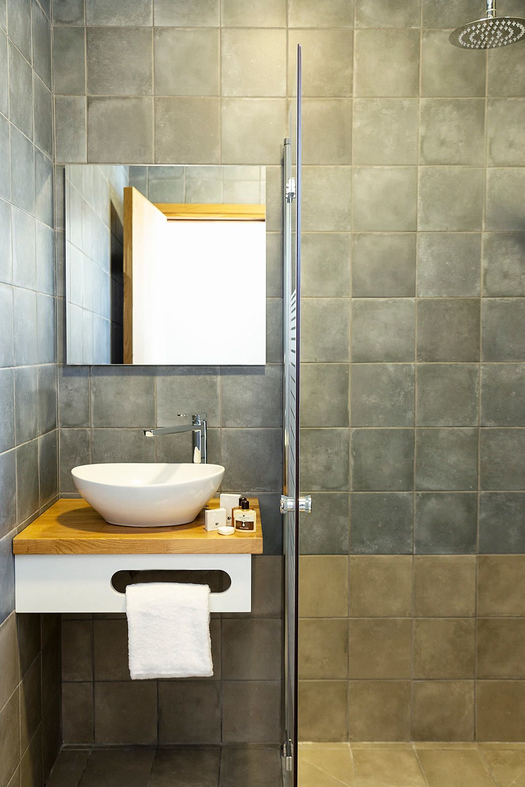 A modern bathroom with a glass shower enclosure, a white vessel sink, and a wooden countertop.