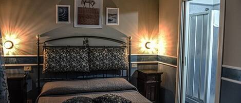 A bedroom with a bed, two bedside lamps, a nightstand, and a door leading to a bathroom.