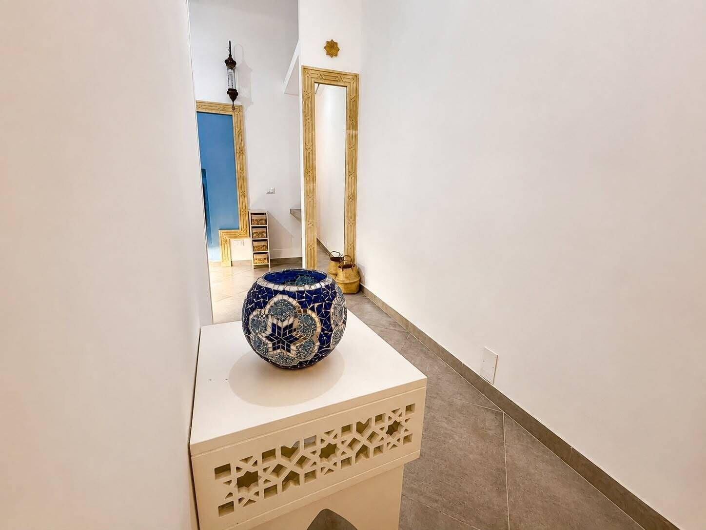 A hallway with a decorative vase on a pedestal, a mirror, and a door.