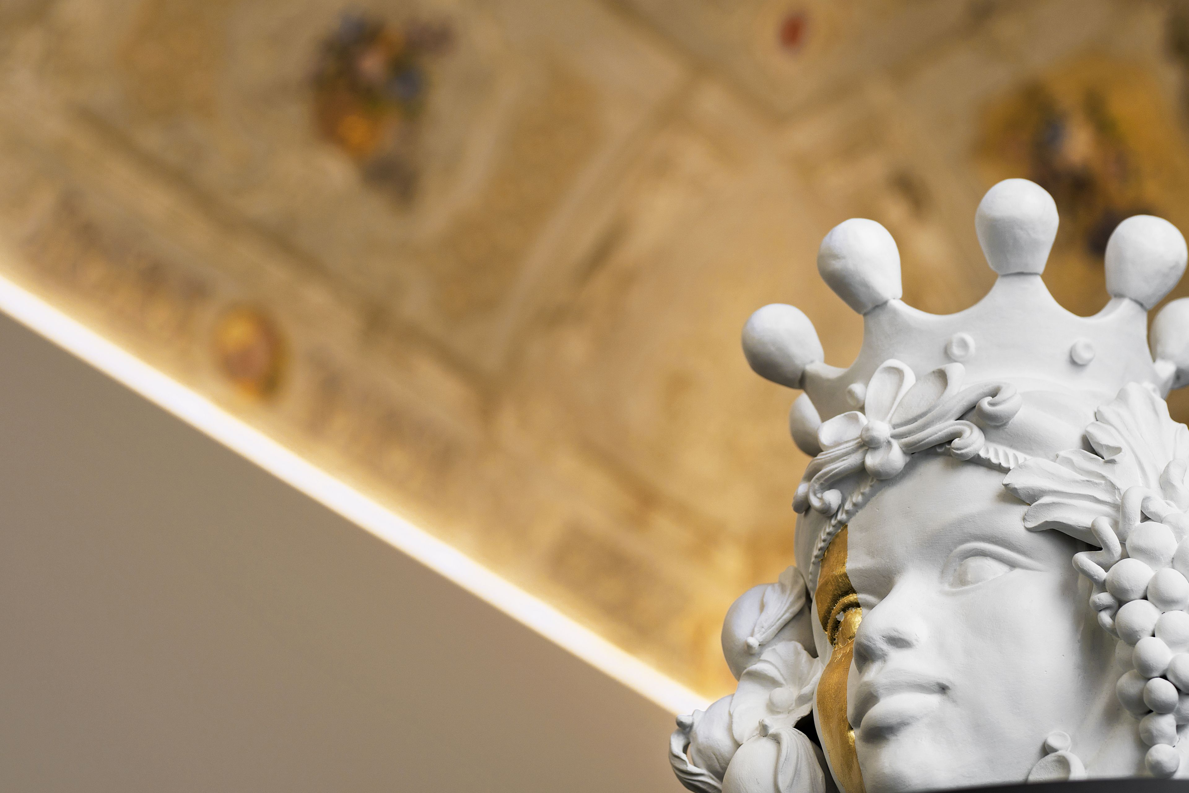 A close-up of a white statue with a crown, set against a golden ceiling with decorative elements.