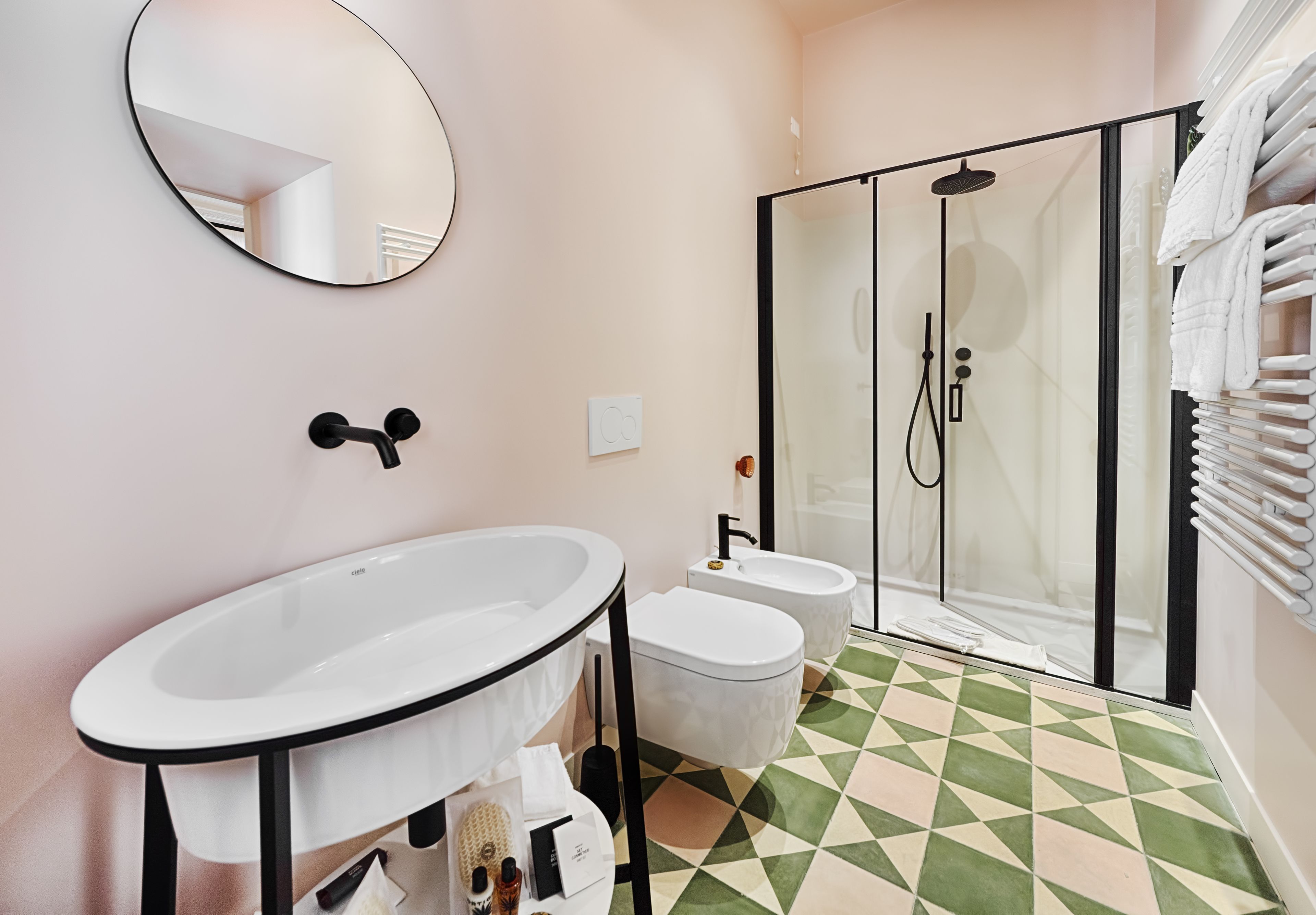 Un baño moderno con un lavamanos ovalado grande, dos inodoros, una ducha con mampara de vidrio y piso de baldosas.