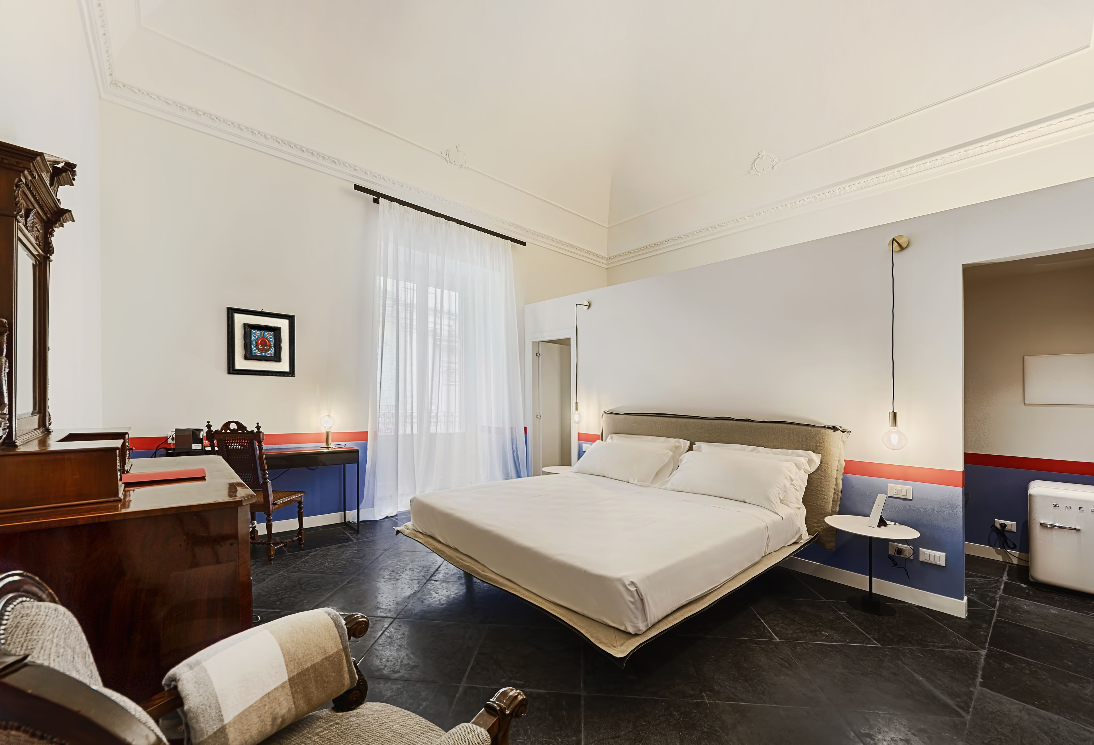 A hotel room with a large bed, a desk, a chair, and a small table.