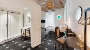 A hotel room with a modern design, featuring a large bed, a desk with a chair, a small round table, and a bathroom with a glass shower enclosure. - a.d. 1768 Boutique Hotel (Ragusa)