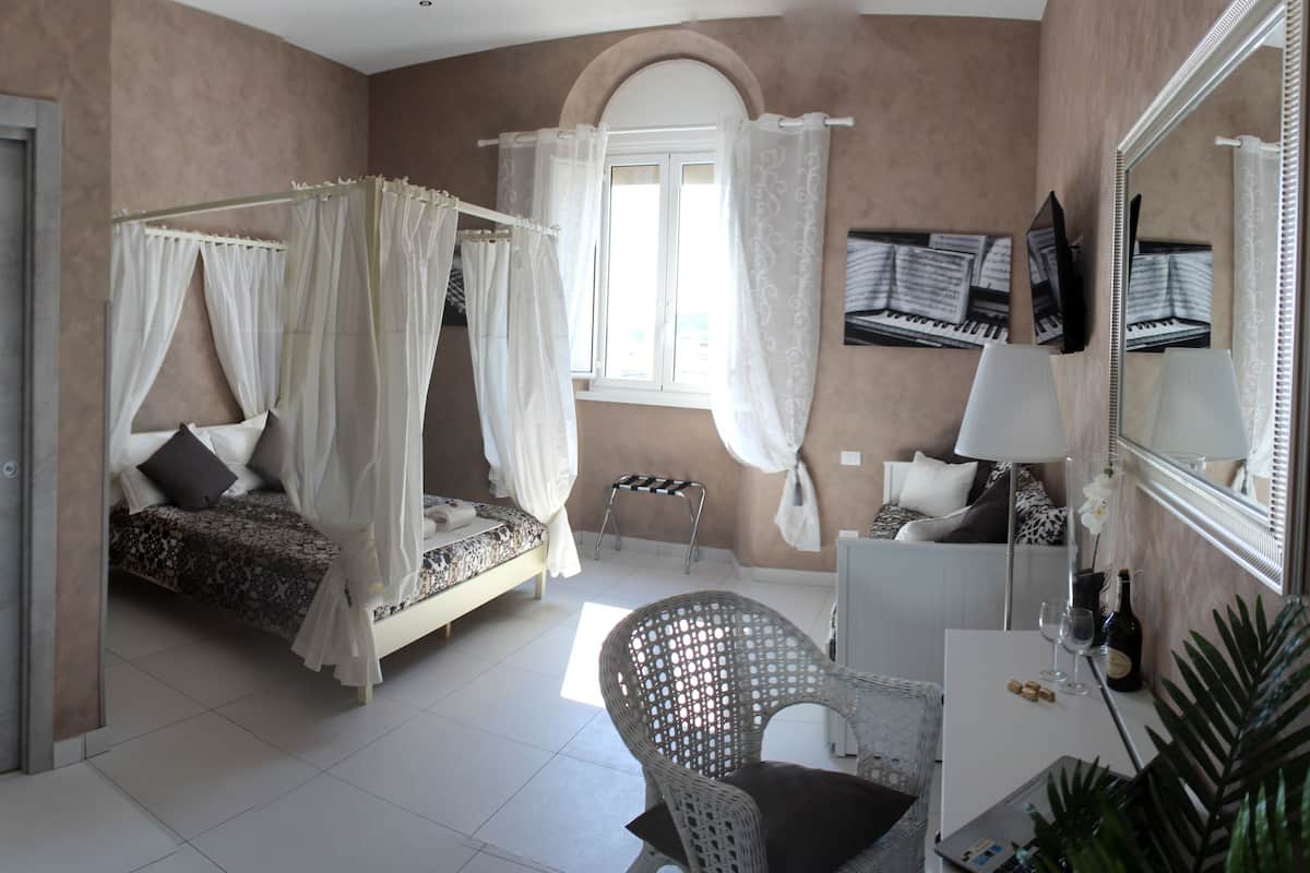 Un dormitorio con cama con dosel, un rincón de descanso con una silla, un escritorio y un espejo.