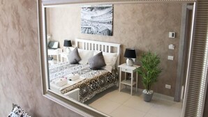 Quarto com cama, mesas de cabeceira, espelho, planta em vaso e quadro na parede.