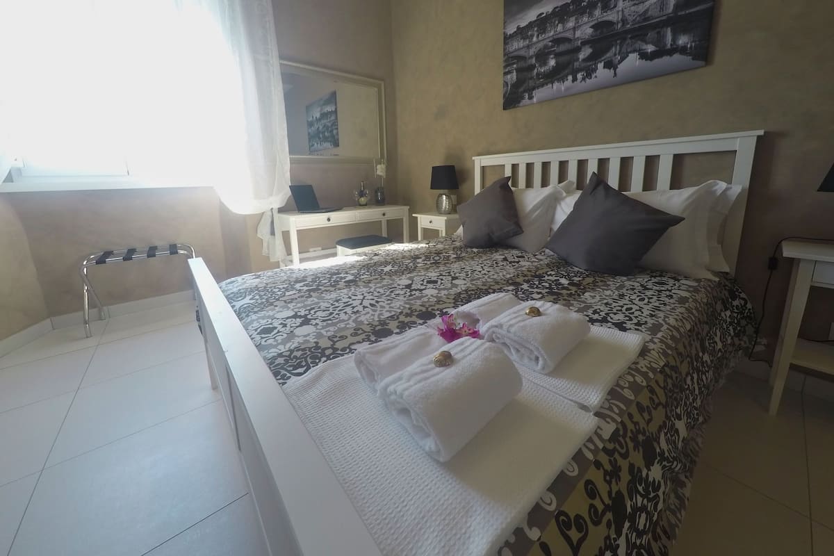 Una habitación de hotel con cama, escritorio, silla, lámpara y un cuadro en la pared.