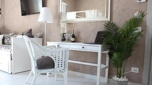 Quarto com cama, escrivaninha branca, cadeira, planta em vaso e espelho.