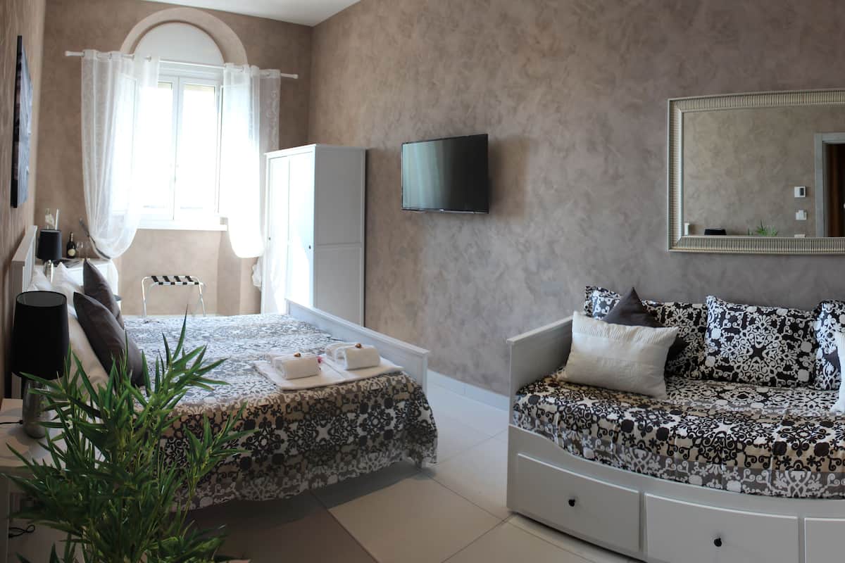 Un dormitorio con cama, sofá, televisor, espejo y ventana con cortinas.
