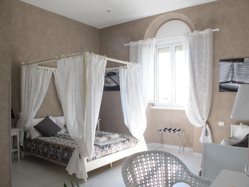 Ein Schlafzimmer mit Himmelbett, einem kleinen Hocker und einem Fenster mit Vorhängen.