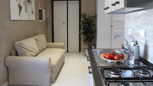 Um espaço compacto com cozinha compacta, sofá, porta e uma obra de arte fixada na parede.