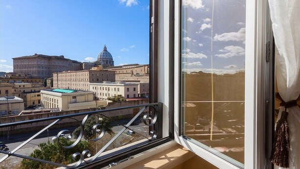 Varanda com vista para um edifício grande com cúpula, outros edifícios históricos e um céu limpo.