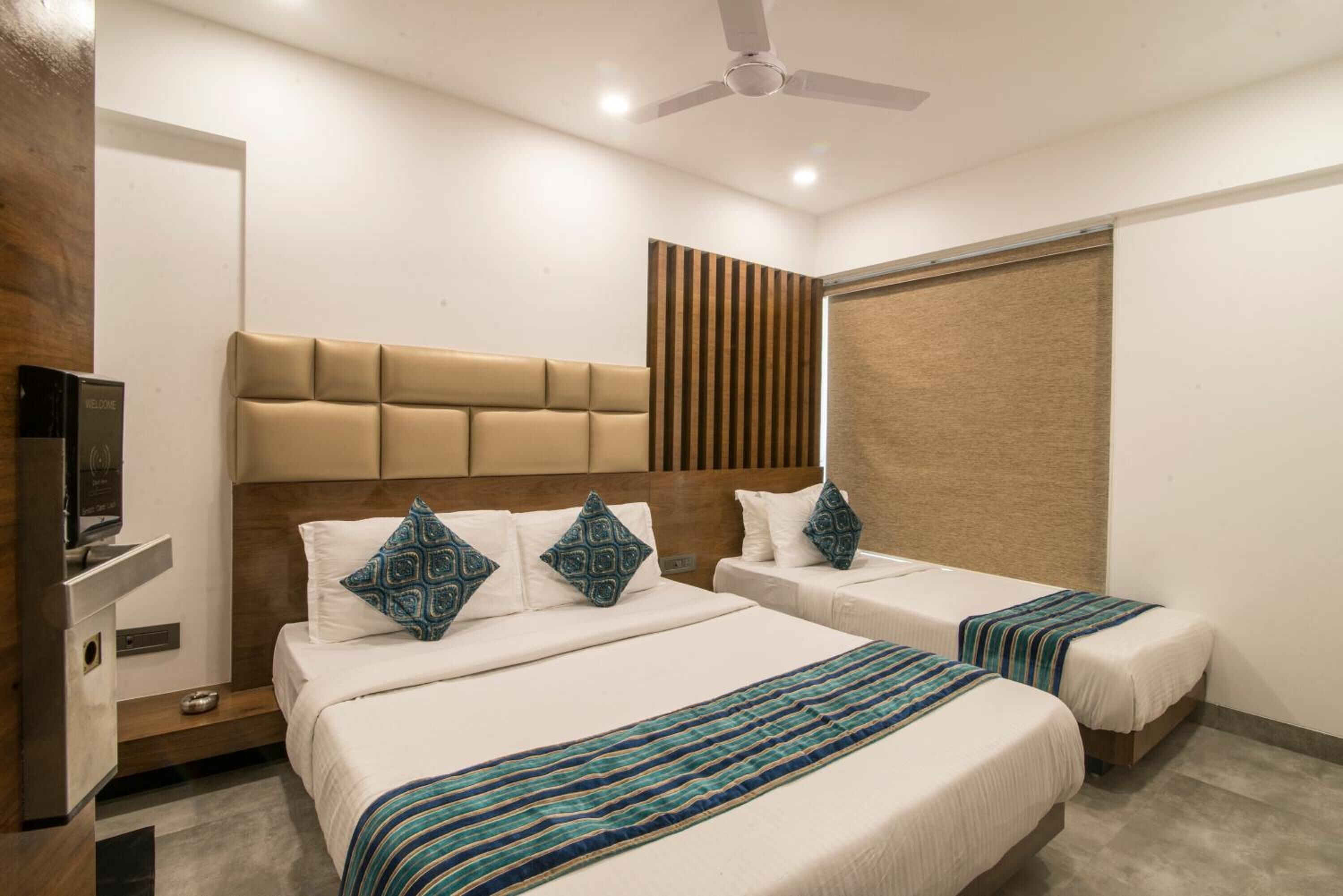 A hotel room with two beds, a headboard, a television, and a ceiling fan.