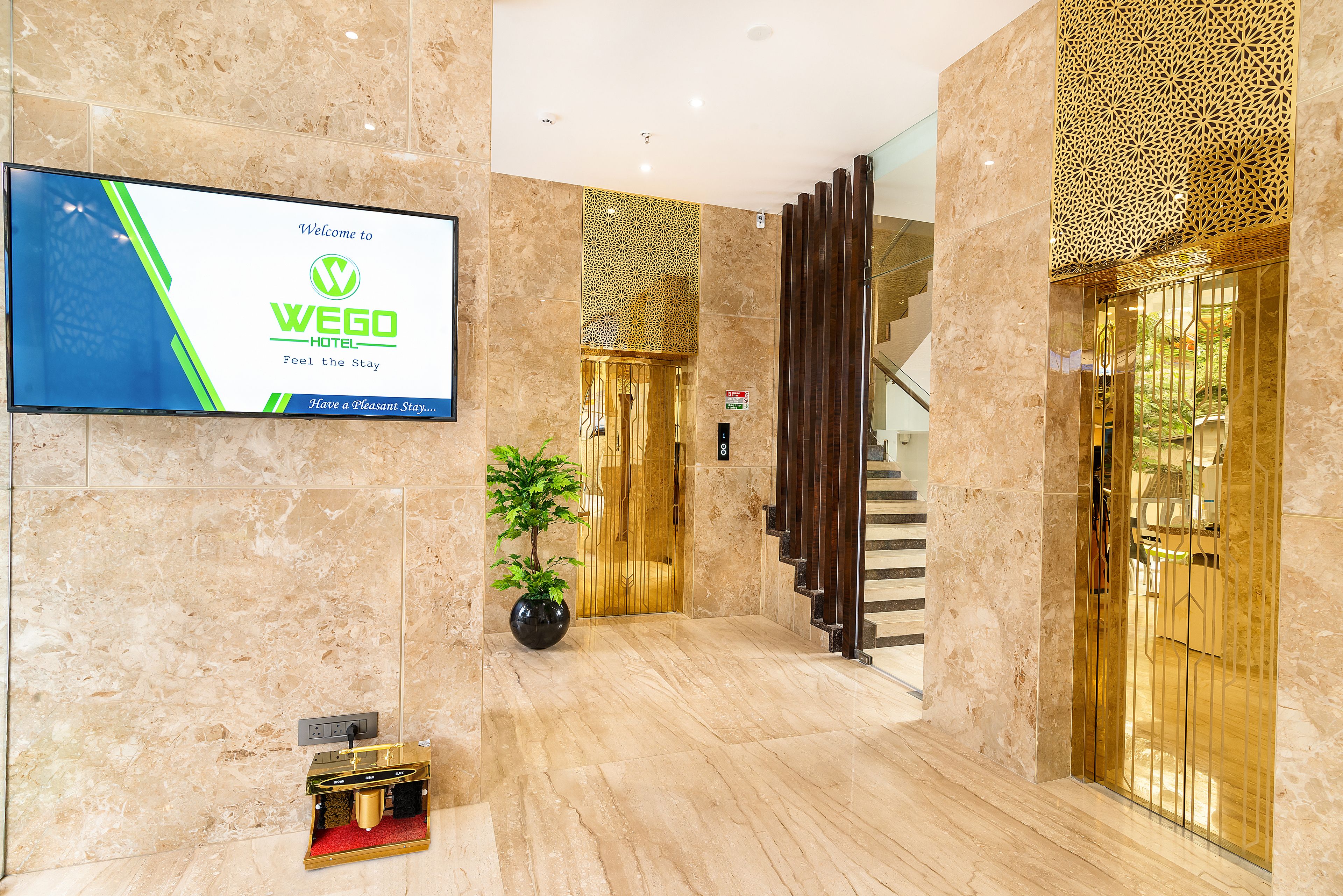 A modern hotel lobby with a marble floor, a reception desk, a potted plant, and a staircase.
