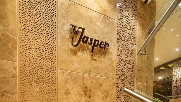 A marble staircase with a handrail leading to a wall with the name 'Jasper' in a decorative script. - Hotel Wego (Mumbai)