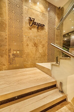 Uma escadaria de mármore com corrimão, conduzindo a uma parede com o nome 'Jasper' em caligrafia decorativa.