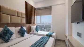 Una habitación de hotel moderna con dos camas, un ventanal con vista a la ciudad, un ventilador de techo y un televisor de pantalla plana montado en la pared.