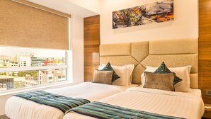 A large bed with a headboard, a ceiling fan, a window with blinds, and a painting on the wall. - Hotel Wego (Mumbai)