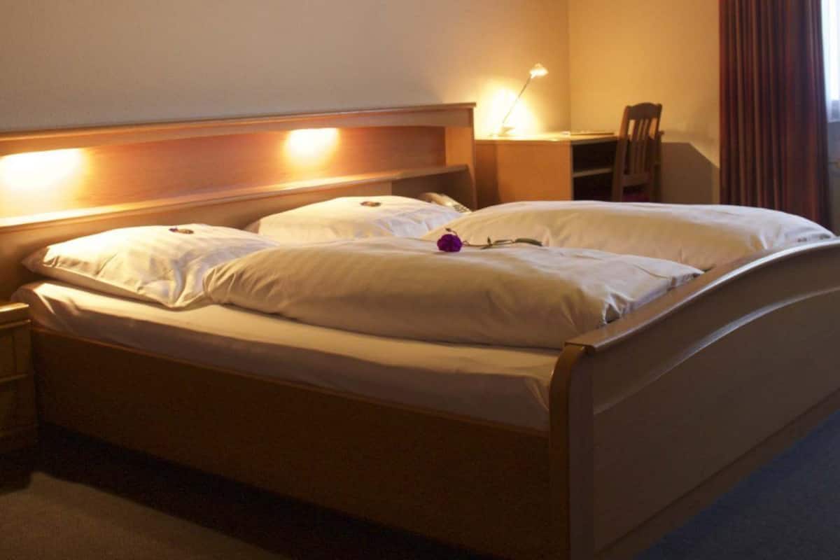 A double bed with white linens, a bedside lamp, and a wooden headboard.