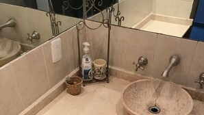 Un bagno con un lavandino grande e rotondo color beige, un cestino, un dispenser per sapone e un portabicchieri.