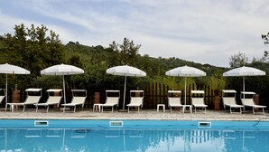 A swimming pool with white lounge chairs and umbrellas, surrounded by greenery. - Il Vecchio Frantoio (Stella Cilento)