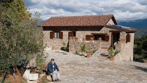 A stone house with a tiled roof, potted plants, and a person sitting on a stone bench. - Il Vecchio Frantoio (Stella Cilento)