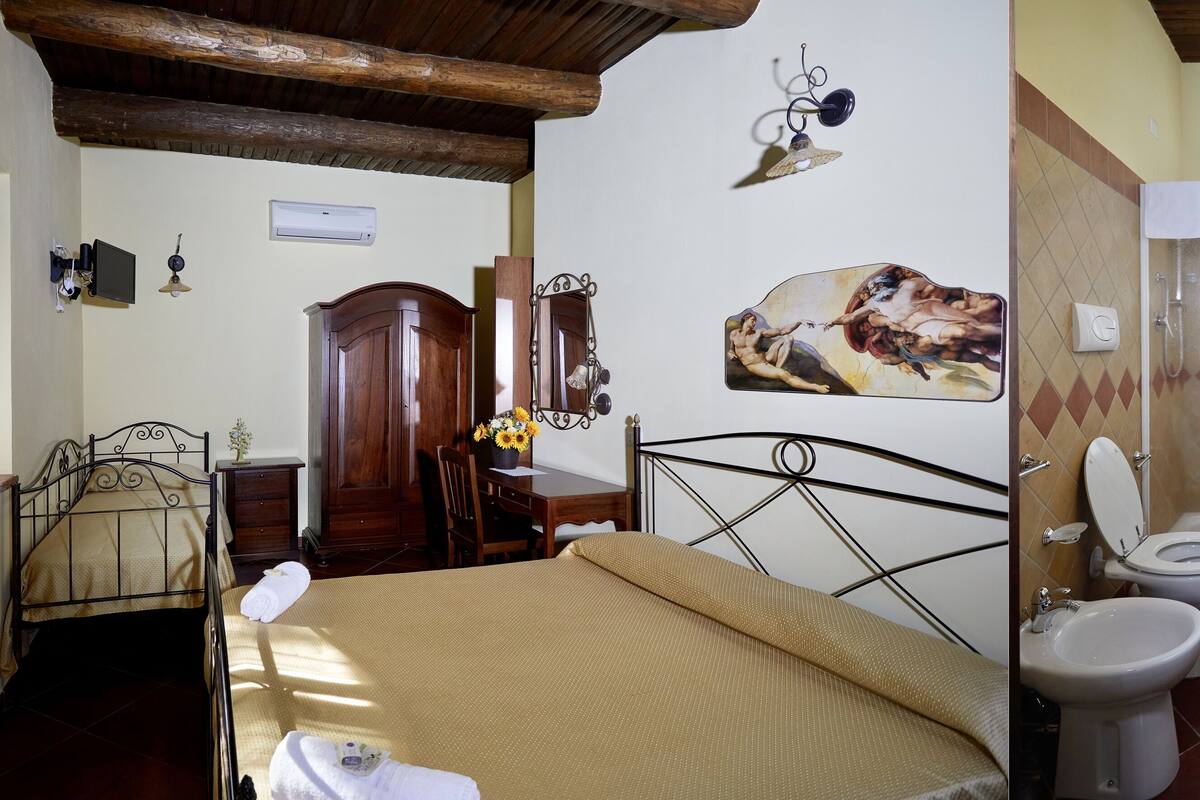 A bedroom with a bed, a desk, a mirror, and a bathroom with a shower, toilet, and sink.