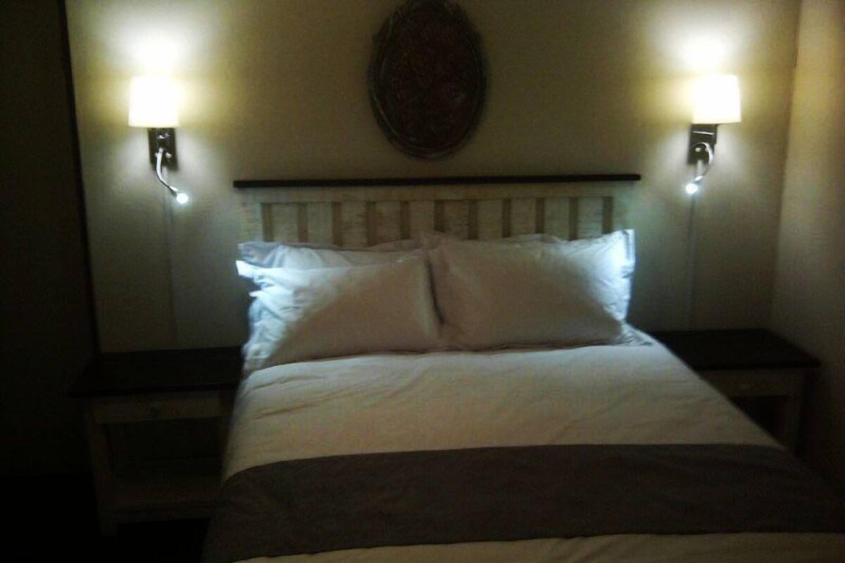 Una cama con ropa de cama blanca y dos lámparas fijadas a la pared.