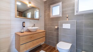 A modern bathroom with a wooden vanity, a white sink, a mirror, a toilet, and a shower area.