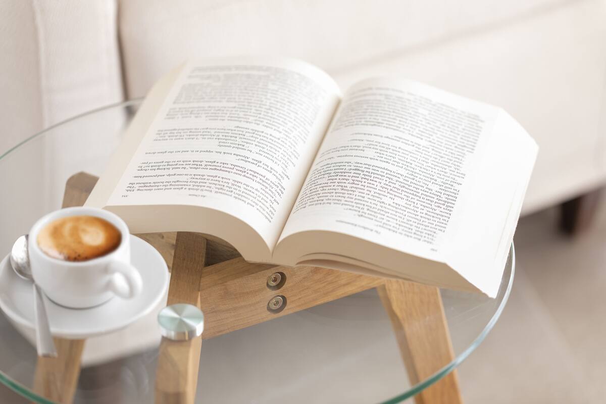 Un libro abierto sobre una mesa de vidrio con una taza de café a su lado.