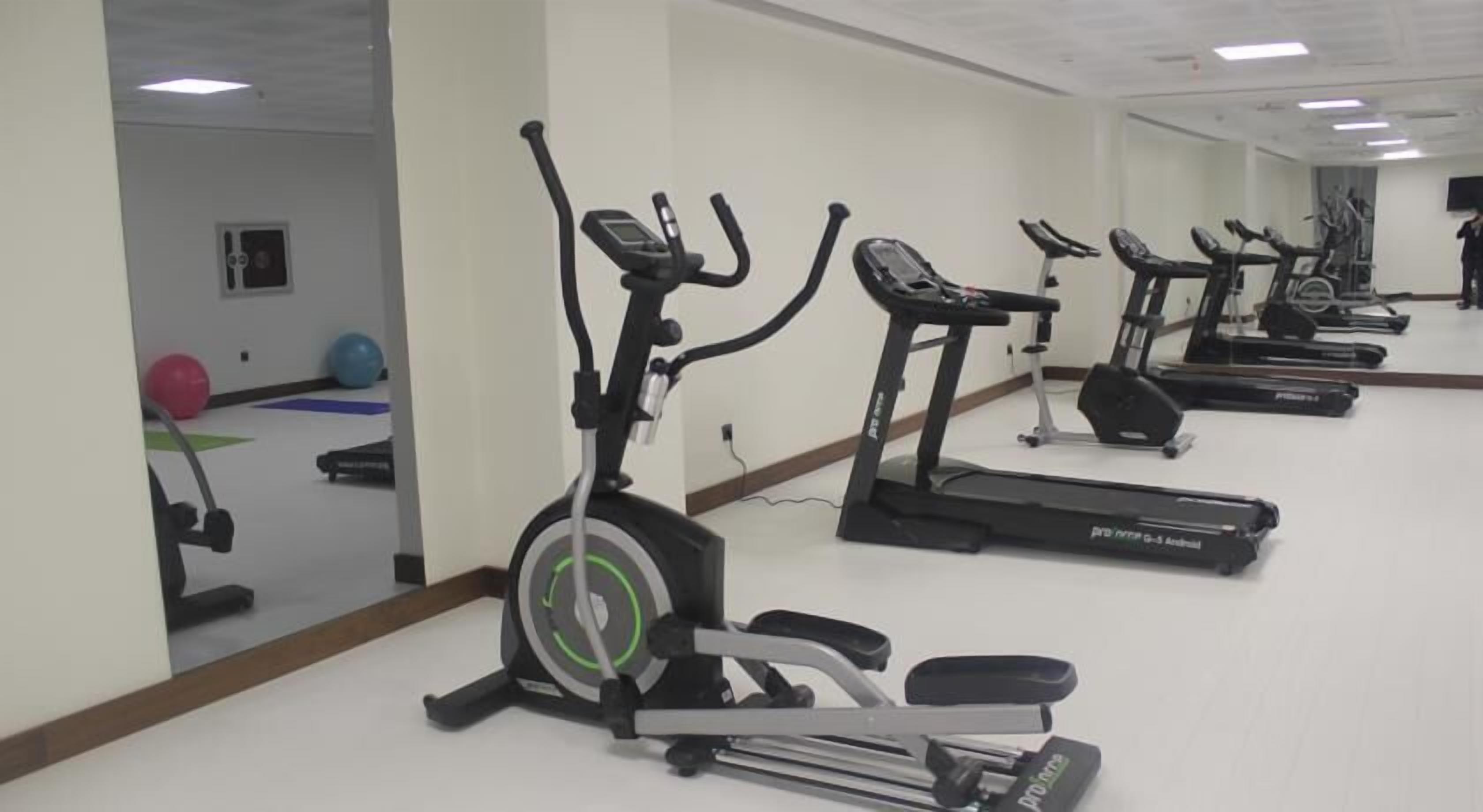 A gym with multiple treadmills and exercise bikes, a mirrored wall, and exercise balls.