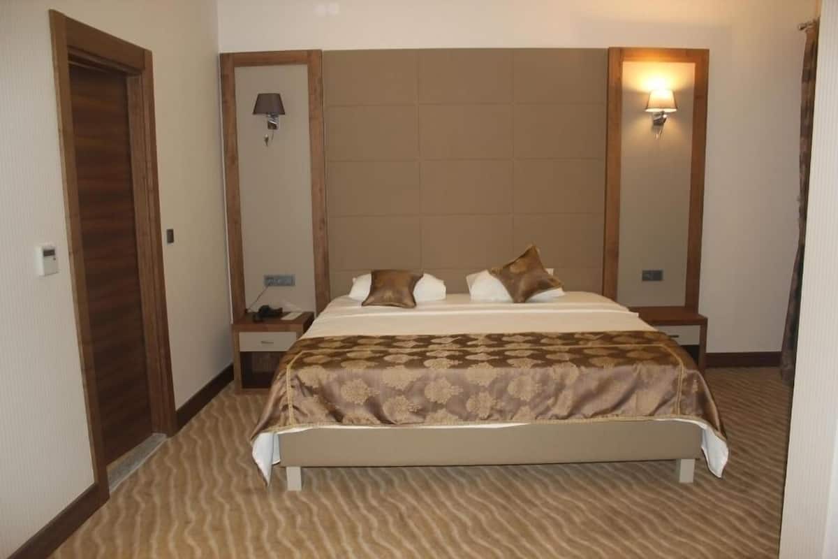 Une chambre d’hôtel avec un grand lit, deux tables de chevet, un miroir et des lampes fixées au mur.