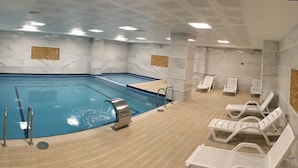 A swimming pool with a wooden deck, lounge chairs, and a tiled wall. - YZE Pirlanta Hotel (Malatya)