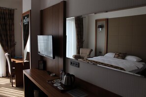A hotel room with a bed, a TV, a desk with a chair, a mirror, and a window with curtains. - YZE Pirlanta Hotel (Malatya)