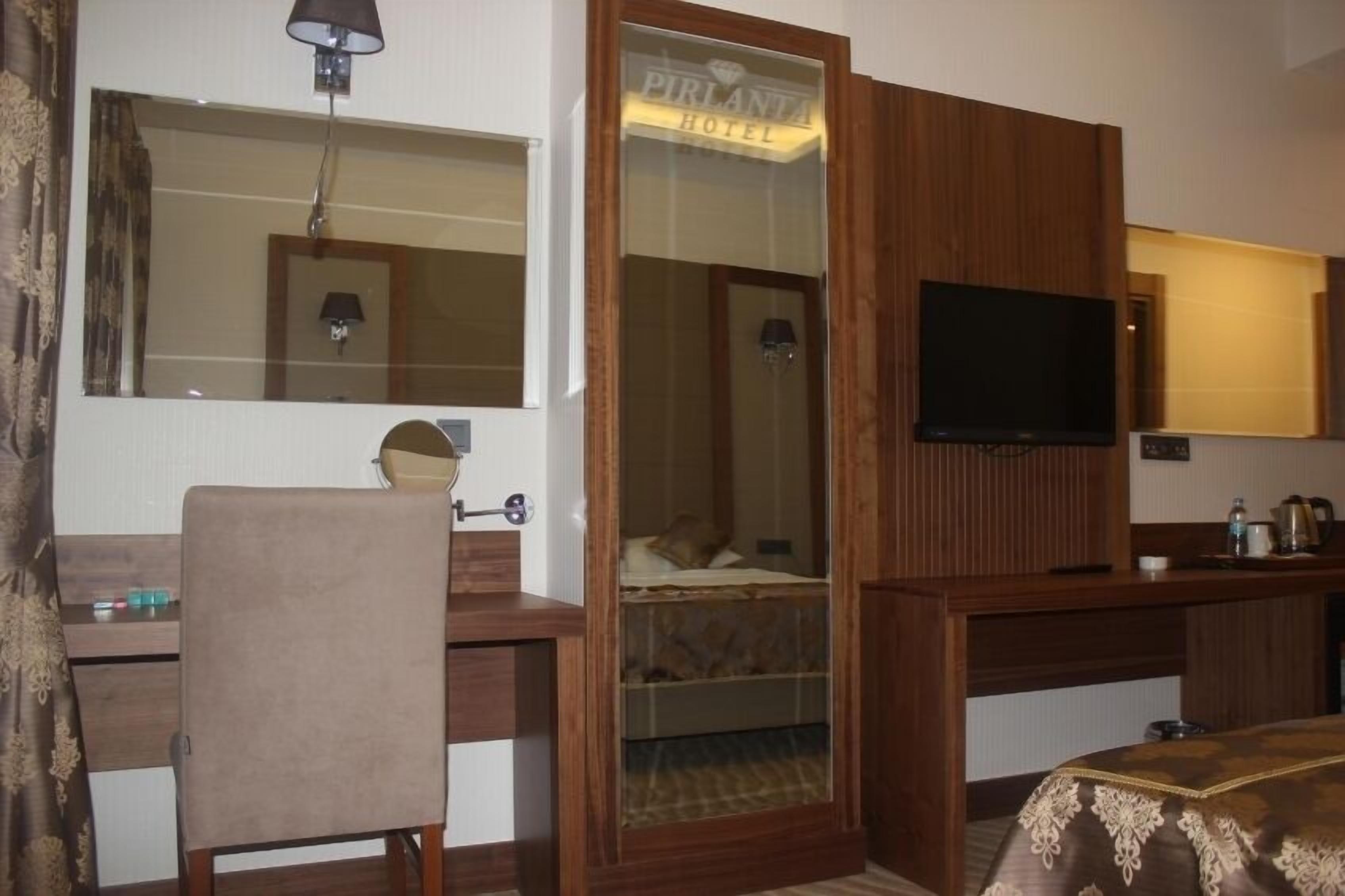 Ein Hotelzimmer mit einem Holztisch, einem Stuhl, einem Fernseher, einem Bett mit Glastür und einem kleinen Tisch mit Lampe.